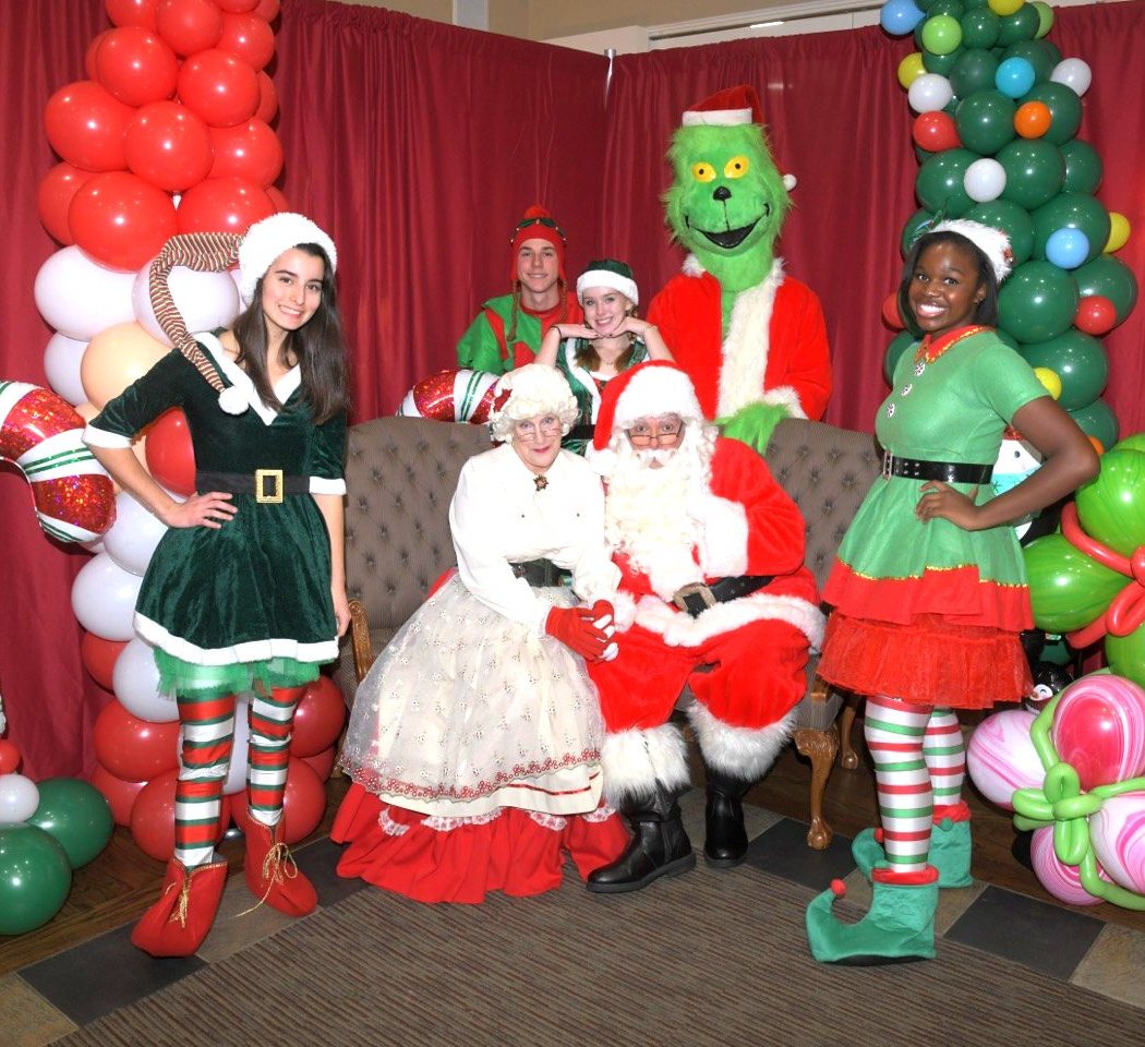 The Grinch, elves, and holiday characters posing with festive balloon decor at a party
