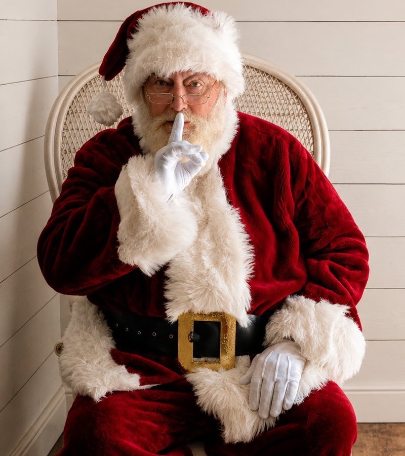 Santa seated in a chair holding a finger to his lips, keeping the surprise